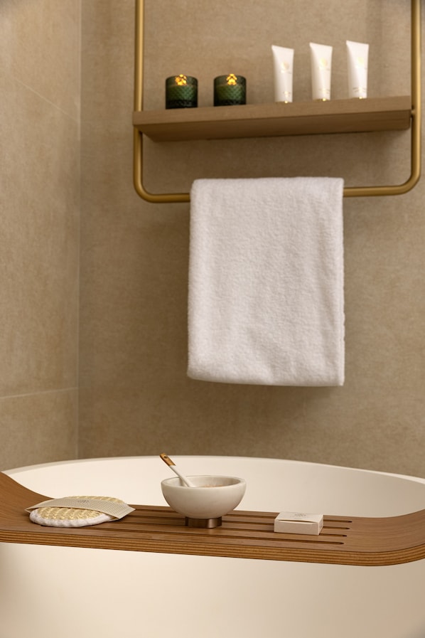 A bathroom with a bathtub, a towel, a soap dish, and toiletries on a shelf.