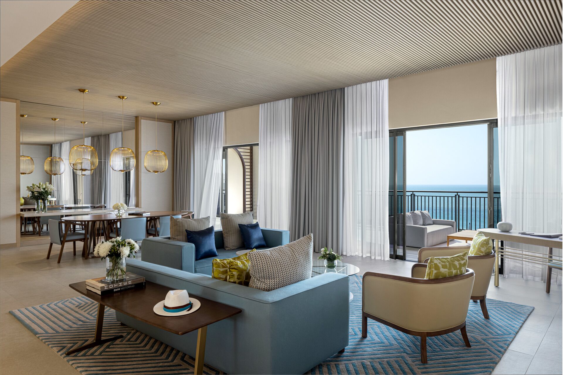 Un vaste espace de vie comprenant un canapé, des fauteuils, une table à manger et un balcon avec vue sur la mer.