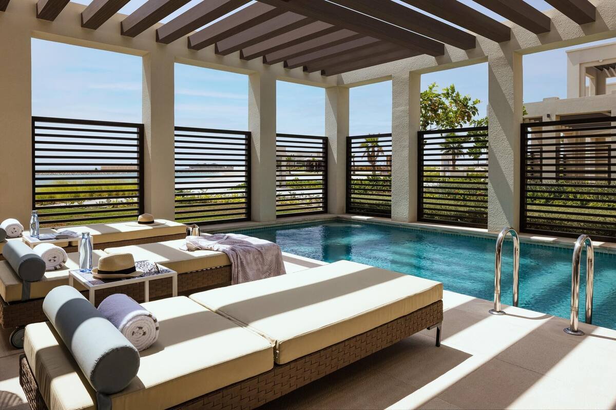 A rooftop pool area with sun loungers, a pool, and a view of greenery.