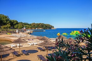 Un resort en la playa con tumbonas, sombrillas de paja y una torre de salvavidas.