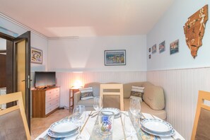 A cozy dining area with a table set for two, a sofa, and a TV in the corner.
