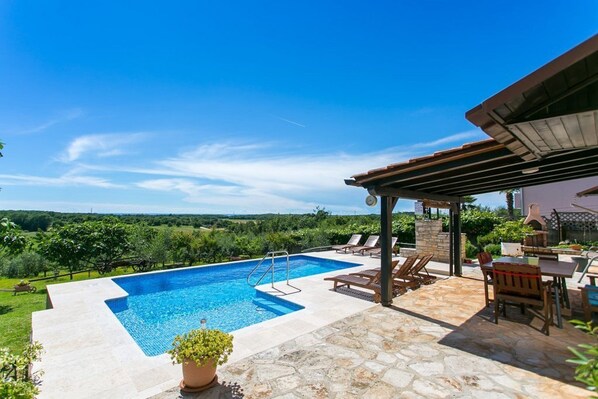 A swimming pool with a stone deck, lounge chairs, and a pergola.
