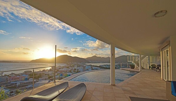 Varanda com vista para o mar e montanhas, piscina e espreguiçadeiras.