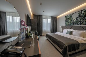 Une chambre d’hôtel avec un lit, un bureau avec un téléphone, une chaise, un verre d’eau, un vase avec des fleurs et un tableau au mur.