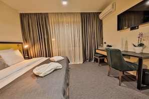 Habitación de hotel con cama, escritorio, silla, televisor y planta en maceta.