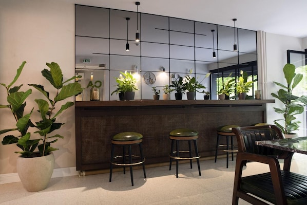 A modern kitchen with a bar area, wicker chairs, and potted plants.
