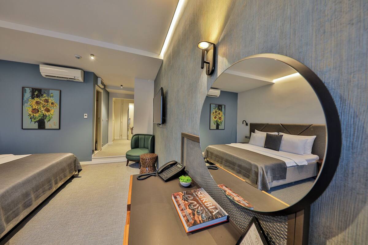 A hotel room with two beds, a desk with a book, a phone, and a mirror.