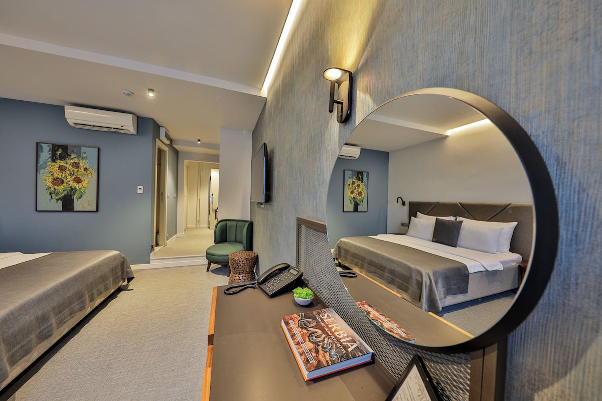 A hotel room with two beds, a desk with a book, a phone, and a mirror.