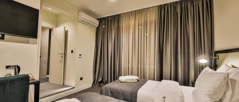 A hotel room with two beds, a desk with a coffee maker, an air conditioning unit, and a large window with curtains.