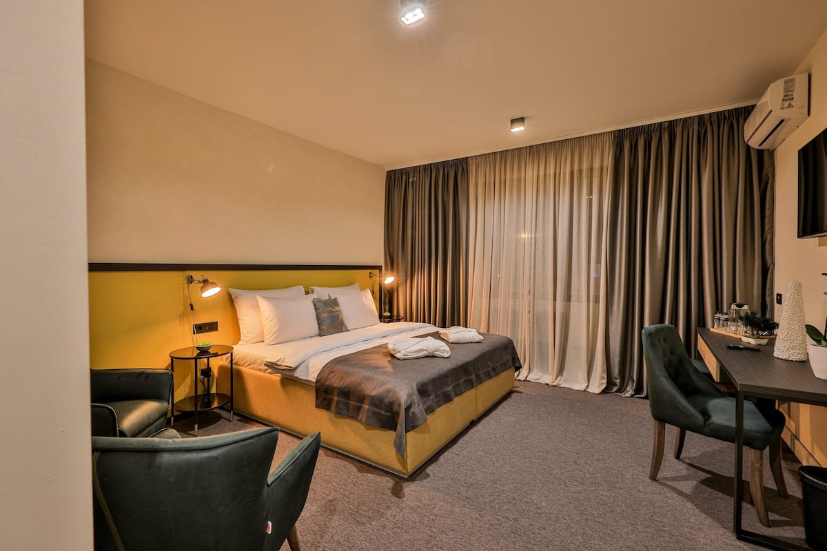 A hotel room with a bed, a desk, a chair, a lamp, and a television.