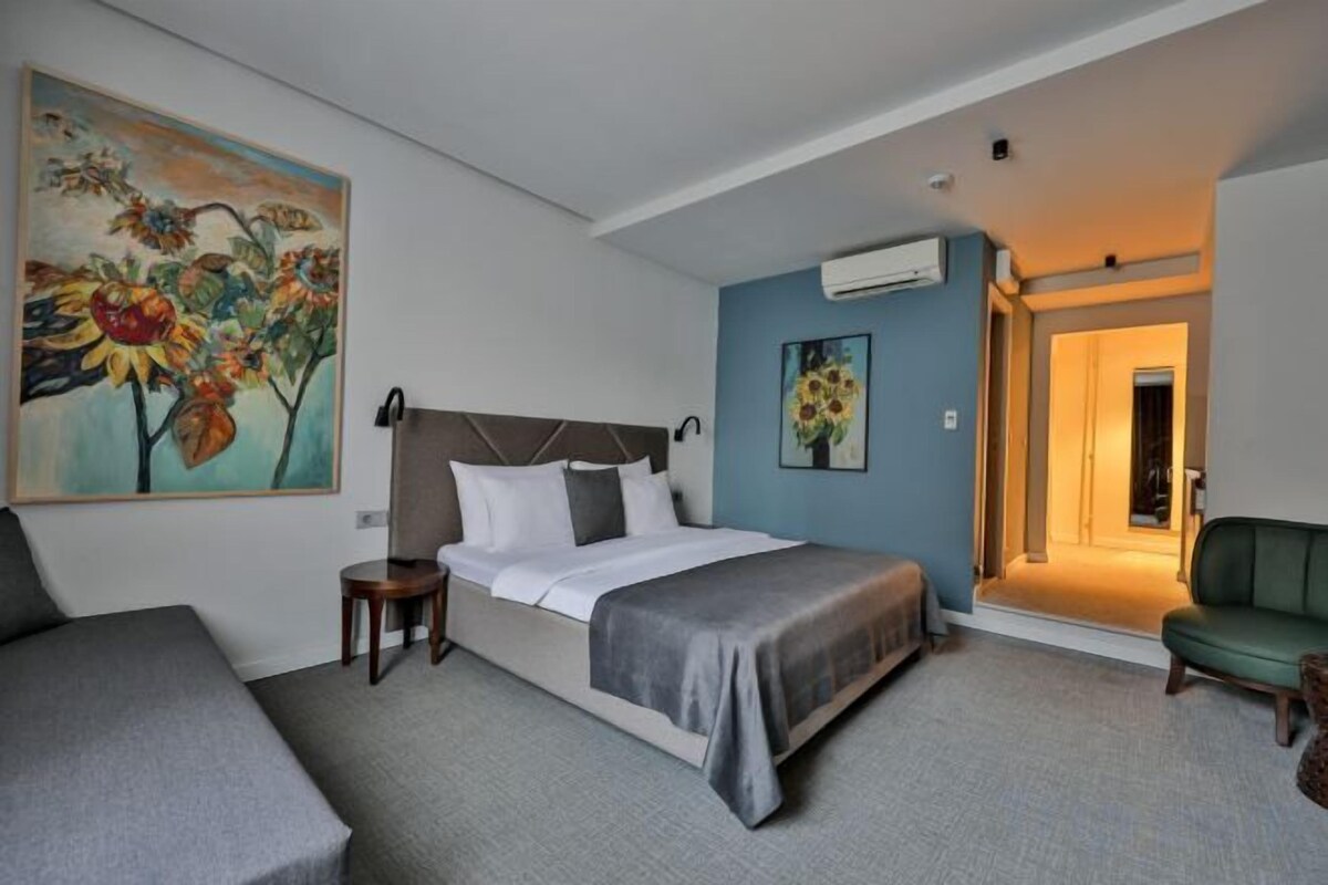 Une chambre d’hôtel avec un lit, un fauteuil vert, une petite table et un tableau accroché au mur.