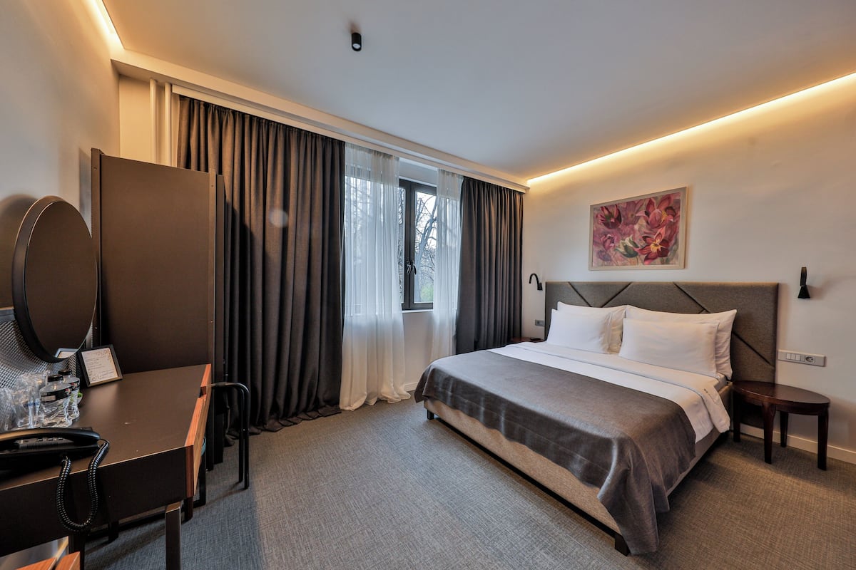 A hotel room with a bed, a desk with a chair, a telephone, and a window with curtains.
