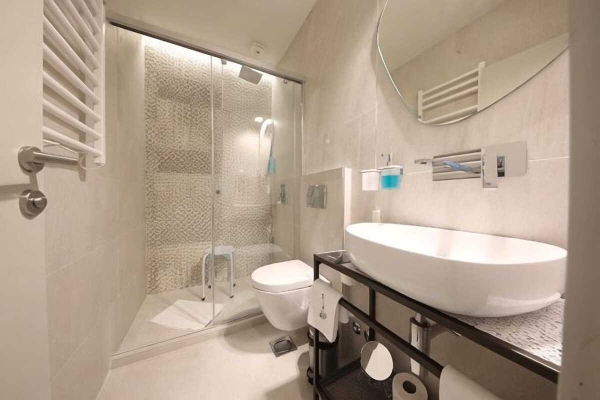 A modern bathroom with a glass shower enclosure, a white sink, and a toilet.