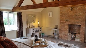 Ein gemütliches Schlafzimmer mit Bett, Schminktisch, Spiegel, Heizkörper, Kamin und einem Fenster mit Vorhängen.