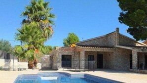 Un bâtiment en pierre avec une piscine, des palmiers et un ciel dégagé.