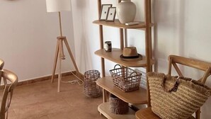 Un coin de pièce avec une chaise en bois, un lampadaire sur trépied, une étagère avec des objets décoratifs et un sac en tissu tissé.