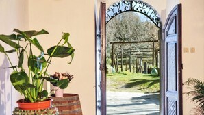 Une porte en bois ouverte donnant sur un jardin agrémenté d’une pergola et d’un sentier.