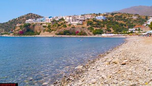 A coastal town with buildings on a hillside overlooking a clear blue sea. - Areti Hotel (Agios Vasileios)