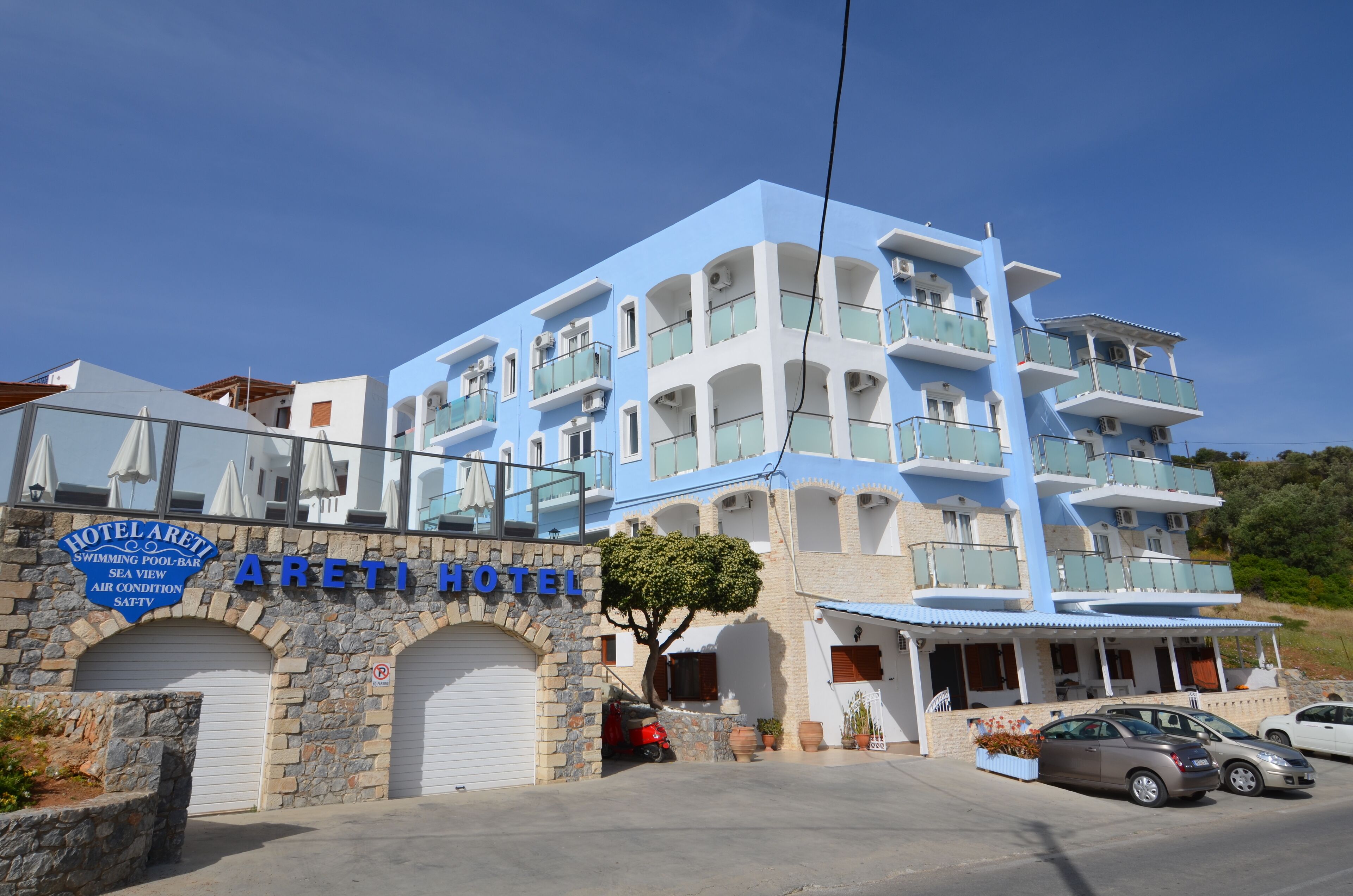 A multi-story hotel with a blue and white facade, a stone archway entrance, and a sign indicating amenities like a swimming pool and air conditioning.