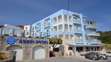 A multi-story hotel with a blue and white facade, a stone archway entrance, and a sign indicating amenities like a swimming pool and air conditioning.