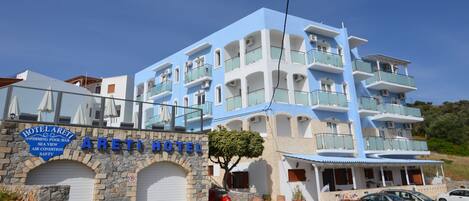 A multi-story hotel with a blue and white facade, a stone archway entrance, and a sign indicating amenities like a swimming pool and air conditioning.