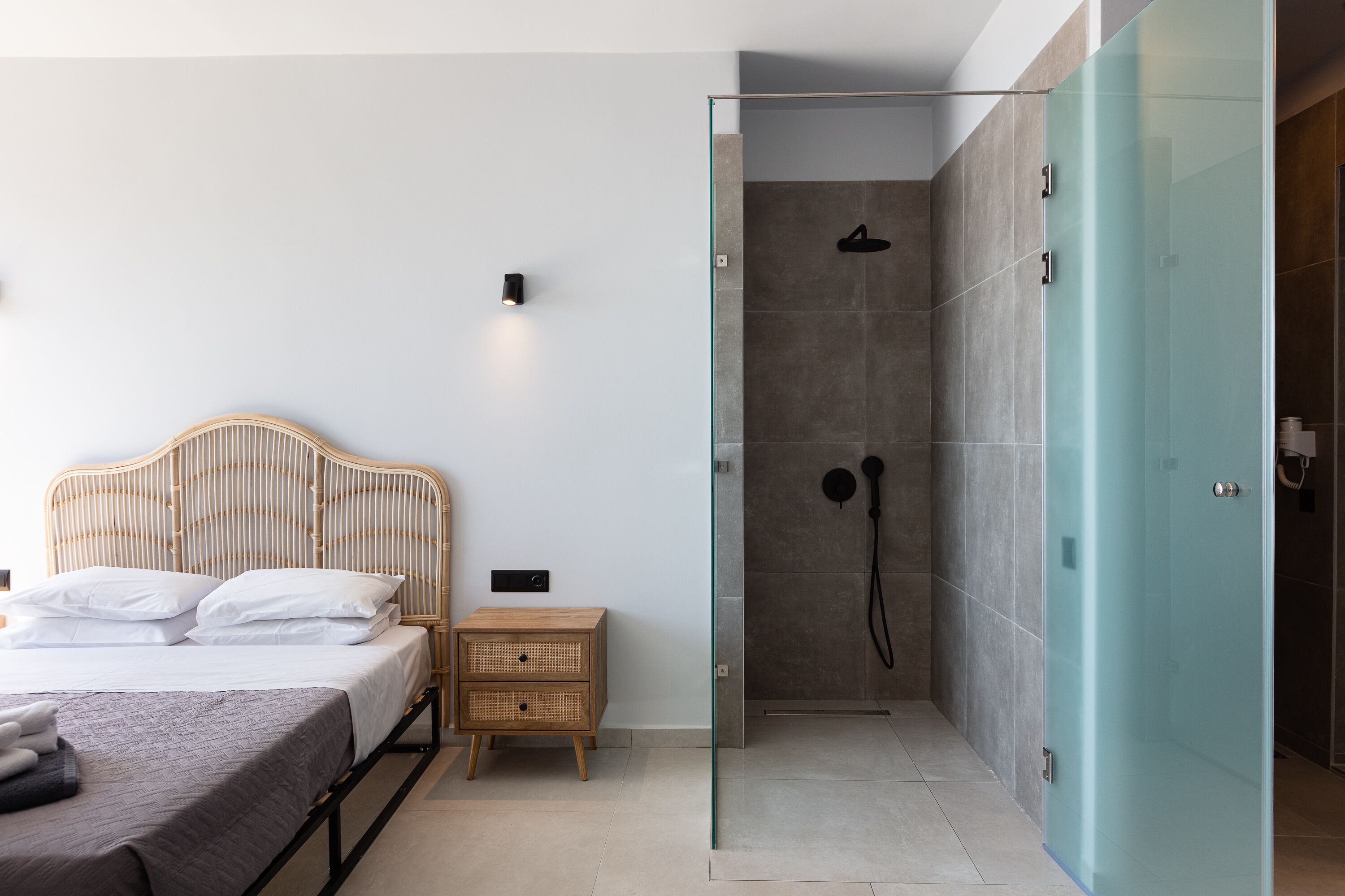 Un dormitorio moderno con cama, mesita de noche y zona de ducha con paredes de cristal.