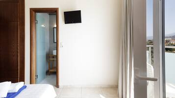 Une chambre d’hôtel avec un lit, une armoire en bois, un téléviseur fixé au mur et un balcon avec des rideaux.