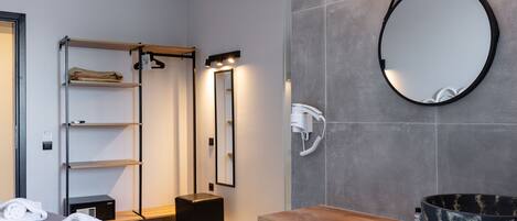 A modern hotel room with a large mirror, a wooden vanity, and a built-in shelf with towels.