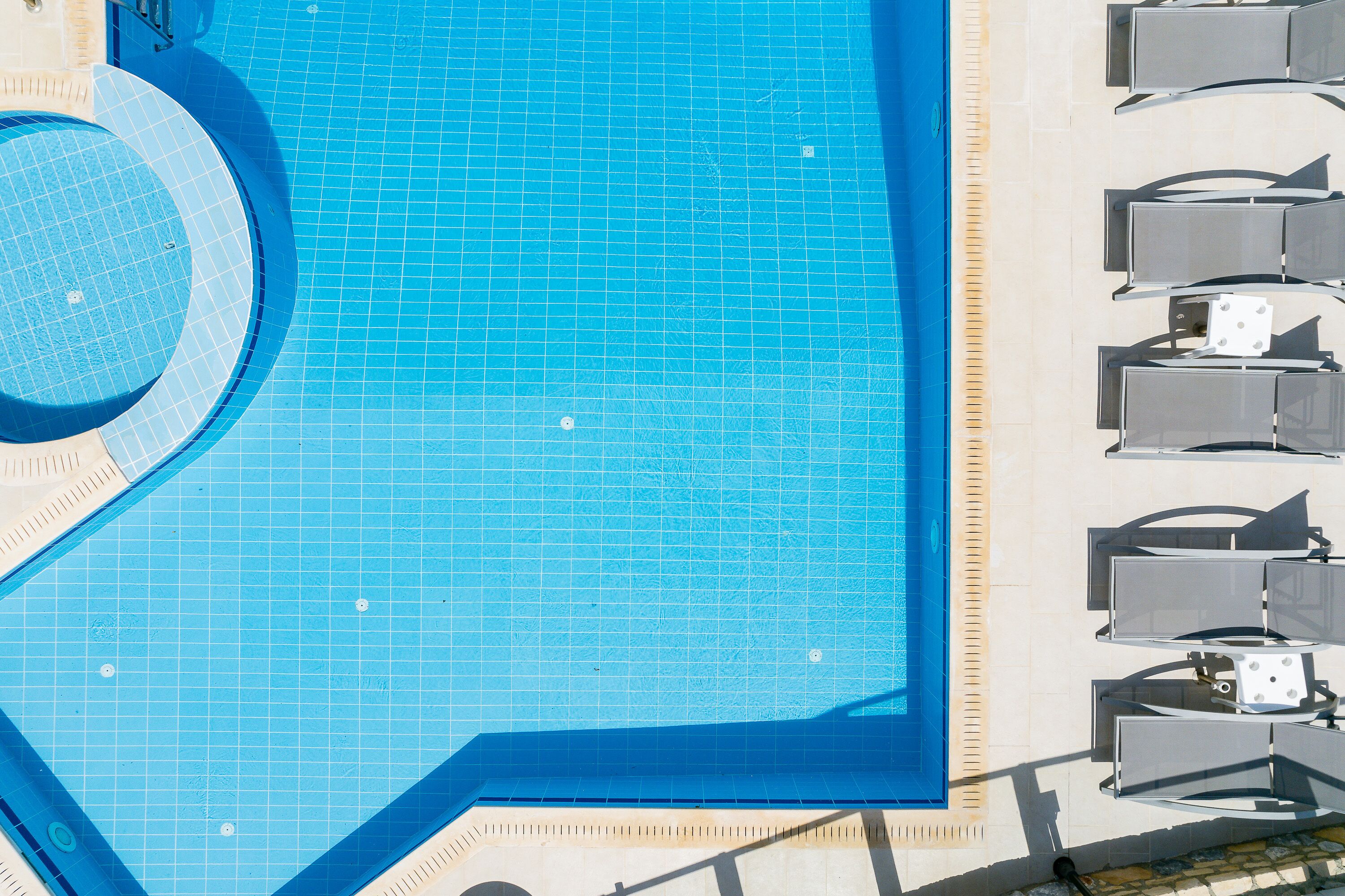 A large, clear blue swimming pool with a tiled deck area and multiple lounge chairs along the poolside.