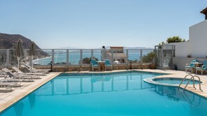 A swimming pool with lounge chairs and tables, a glass balustrade, and a view of the sea and mountains. - Areti Hotel (Agios Vasileios)