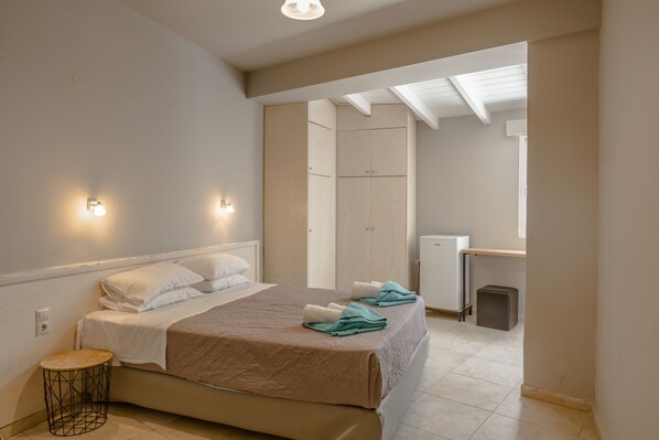 A bedroom with a bed, bedside lamps, a small round table, and a wardrobe. - Areti Hotel (Agios Vasileios)