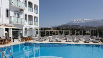 A pool area with lounge chairs and a view of a mountain.