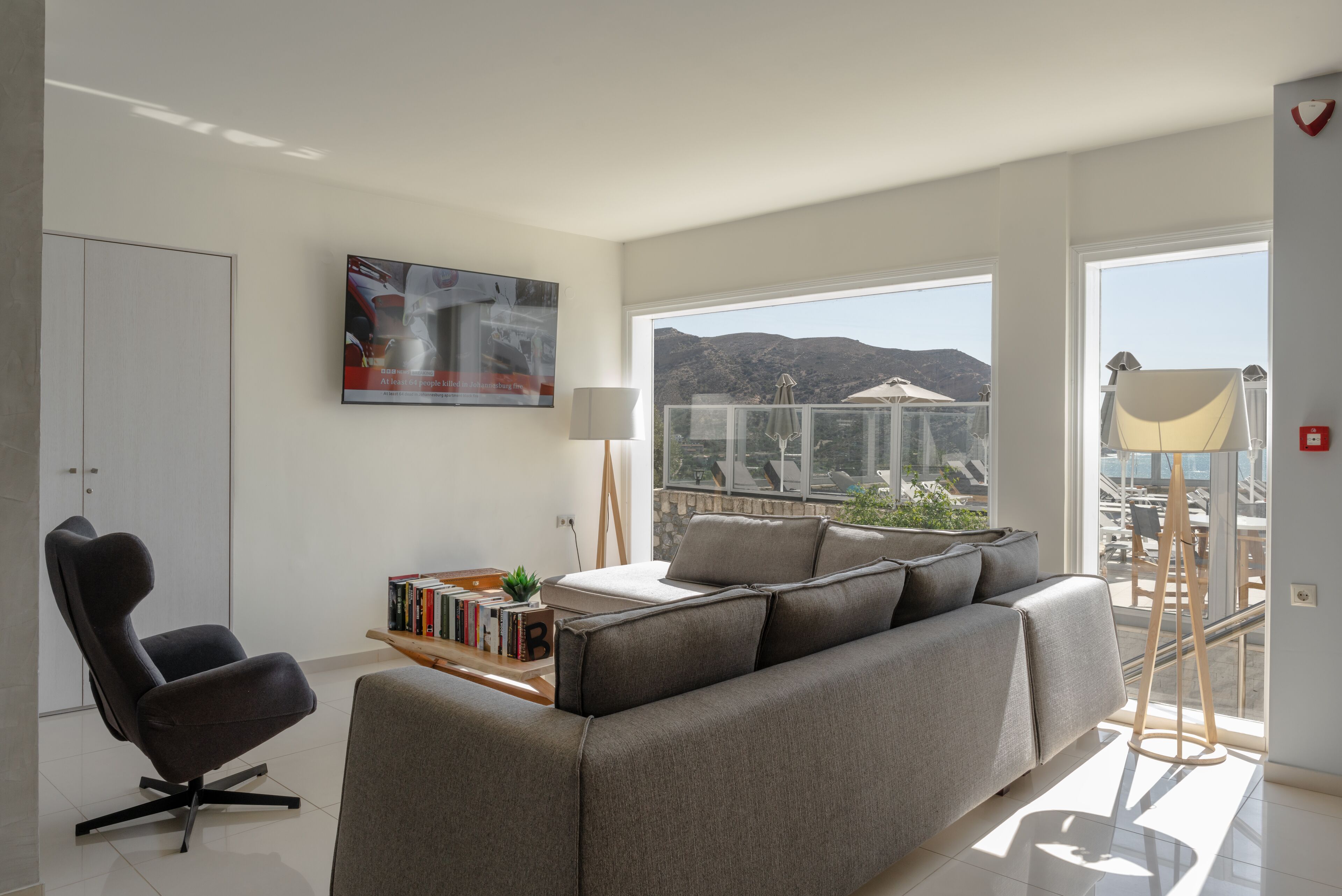A modern living room with a grey sofa, a black chair, a bookshelf, and a large window offering a view of mountains.