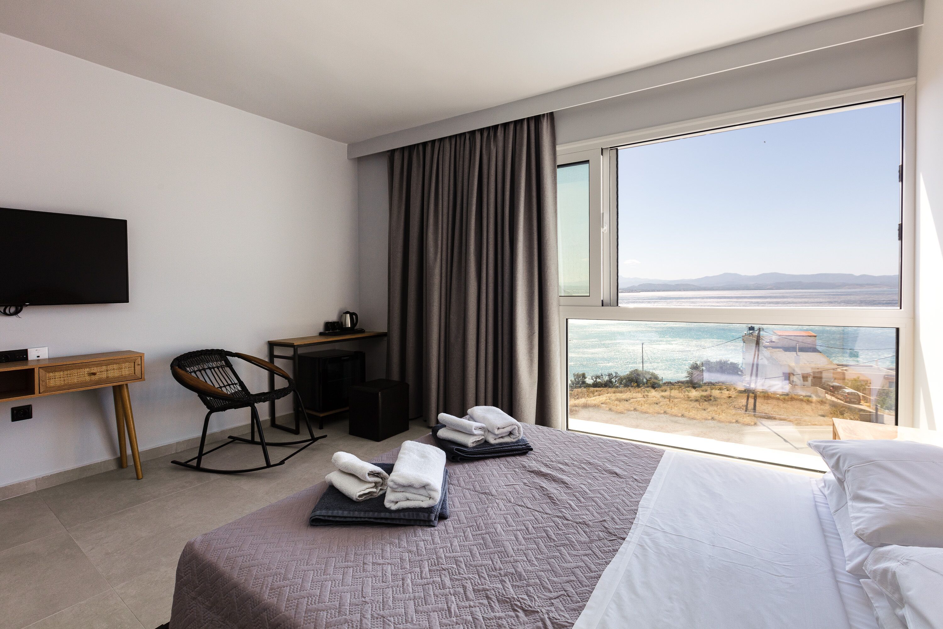 Una habitación de hotel con cama, escritorio, silla y un amplio ventanal con vista al mar.