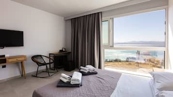 Una habitación de hotel con cama, escritorio, silla y un amplio ventanal con vista al mar.