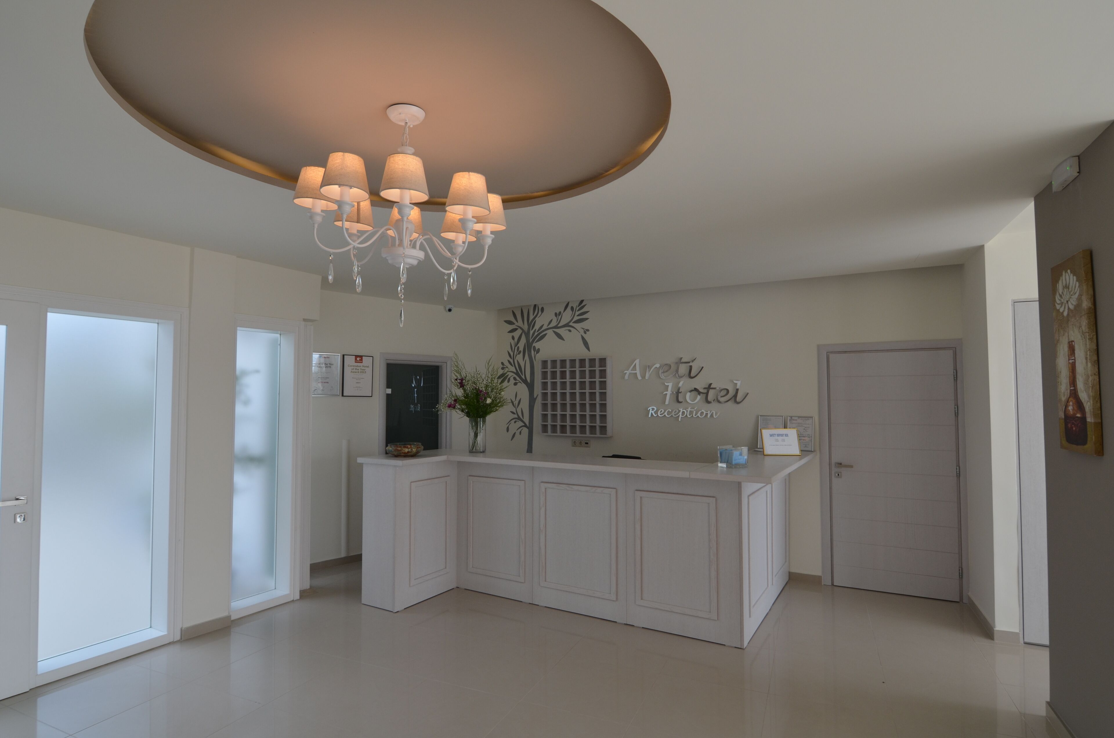 A hotel reception area with a modern design, featuring a central reception desk, a chandelier, and a wall-mounted sign that reads "Arety Hotel Reception".