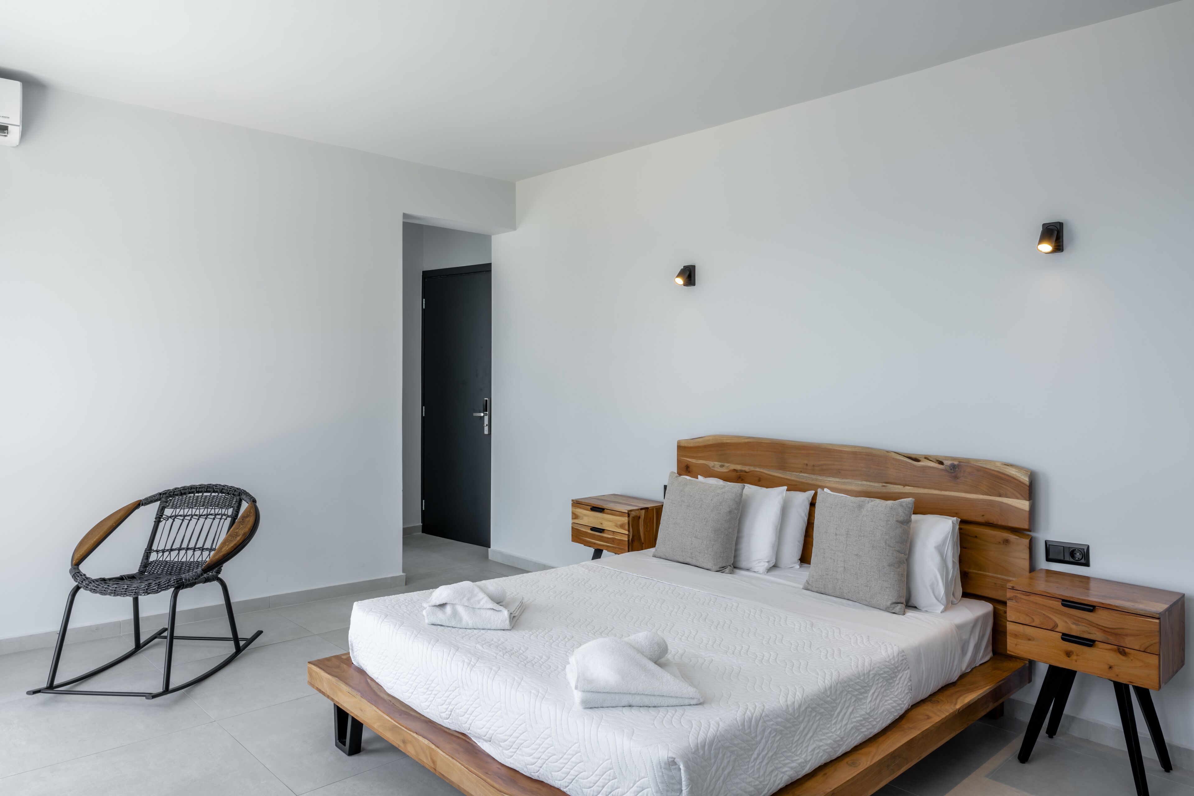 A modern bedroom with a wooden bed, white bedding, a rocking chair, and two bedside tables.