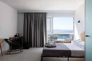 A modern hotel room with a bed, a chair, a desk, and a view of the sea. - Areti Hotel (Agios Vasileios)