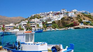A coastal town with buildings on a hillside, boats docked in the water, and a clear blue sky. - Areti Hotel (Agios Vasileios)