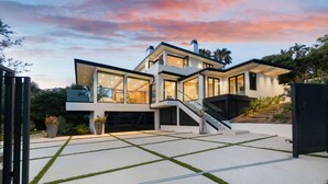 A modern two-story house with large glass windows, a covered outdoor area, and a staircase leading to the upper level.