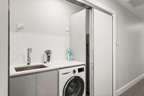 A compact laundry room with a washing machine, a sink, and a drying rack.