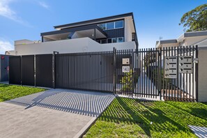 A modern two-story building with a gated entrance, numbered parking spaces, and a well-maintained lawn.