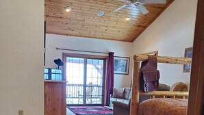 Una habitación con techo de madera, un ventilador de techo, una cama, un sofá, un tapete de cuero y vistas al exterior a través de un cristalero corredizo.