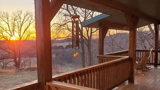 Una terraza de madera con barandilla, un móvil colgante y vistas del atardecer.