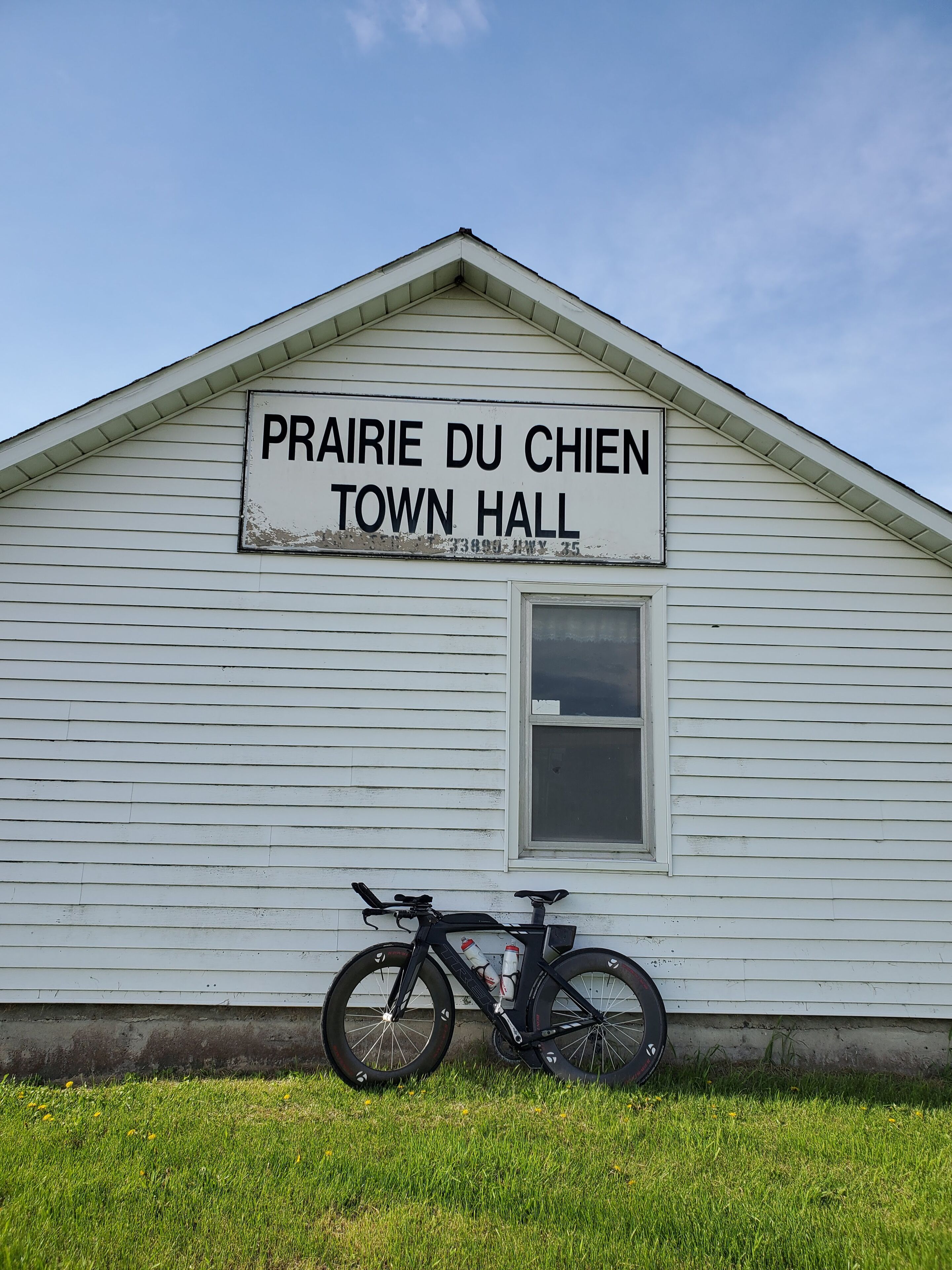 A white building with a sign reading "Prairie du Chien Town Hall." A bicycle is parked in front.