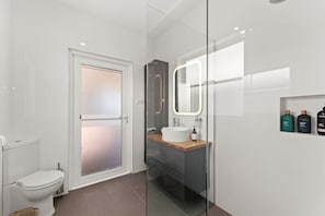 Een moderne badkamer met toilet, een douchecabine met glazen wanden, een wastafel met spiegel en toiletartikelen aan de muur.