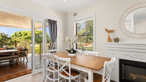 A dining area with a wooden table and white chairs, a potted orchid, and a fireplace with decorative items. - Moorooba Pet Friendly Holiday Home Nelson Bay (Nelson Bay)