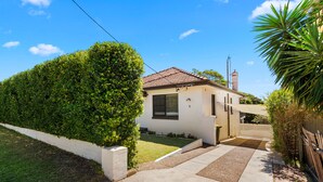 A residential house with a white exterior, a tiled roof, and a well-maintained front yard with a hedge and a small garden. - Moorooba Pet Friendly Holiday Home Nelson Bay (Nelson Bay)