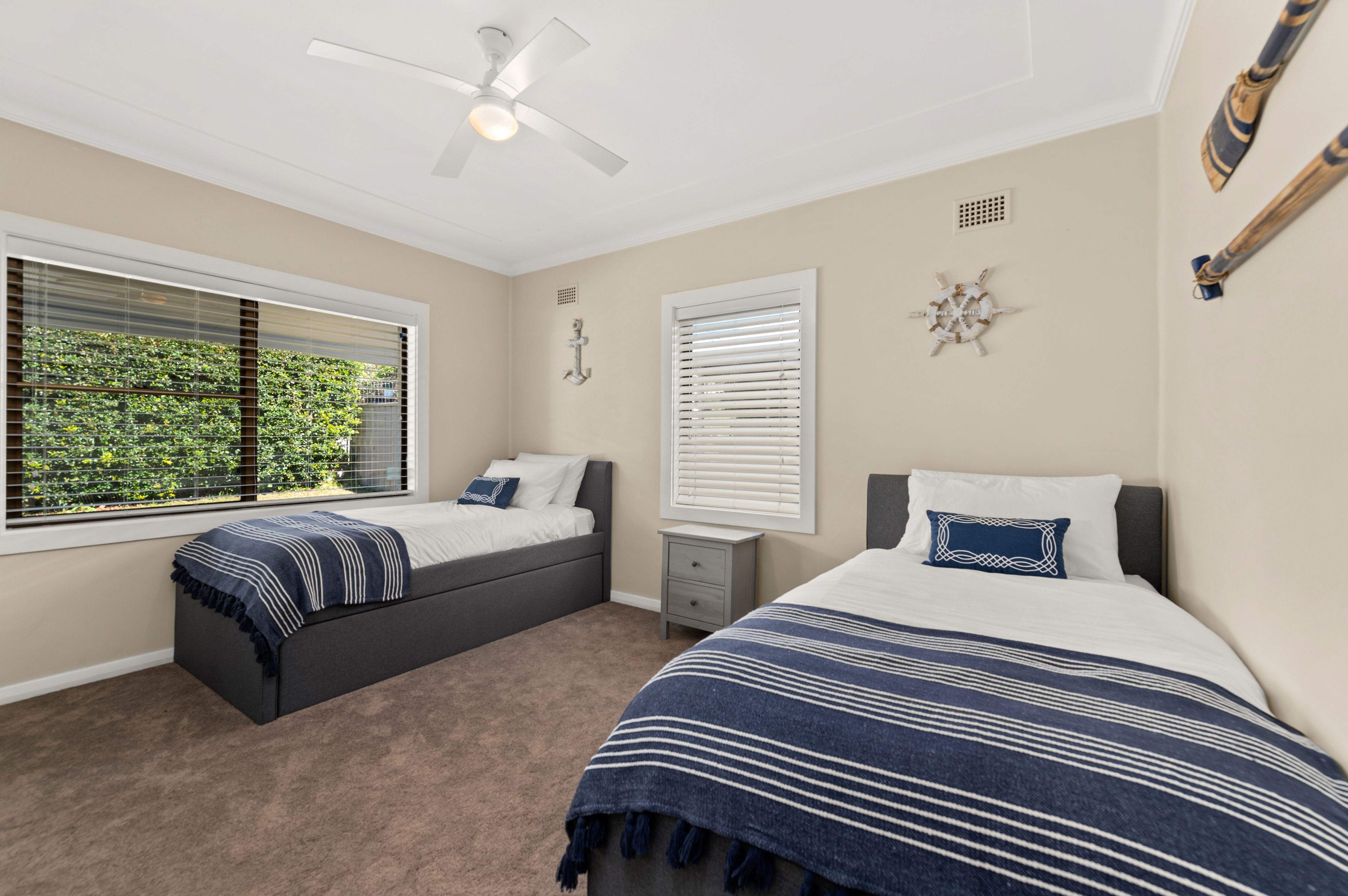 A bedroom with two beds, a ceiling fan, and a window with blinds.