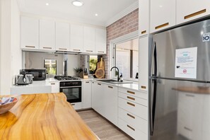 A modern kitchen with white cabinetry, a stainless steel refrigerator, and a wooden dining table.